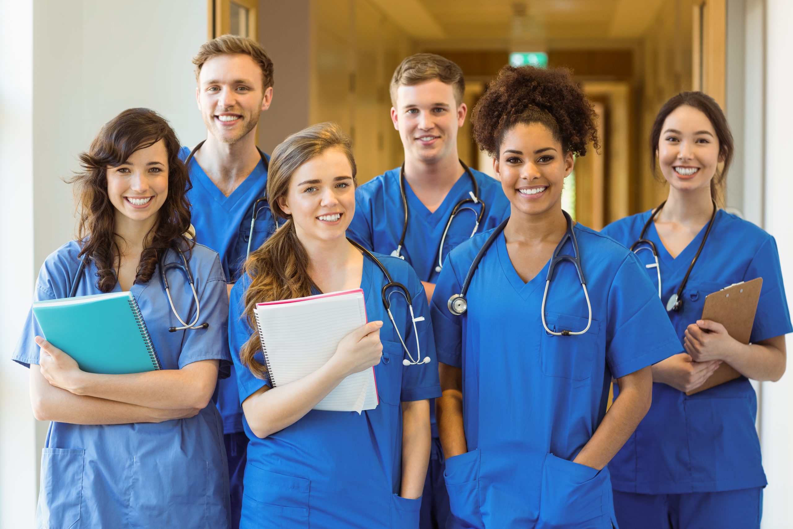 6 medical students wearing blue scrubs smiling with text books and stethoscopes